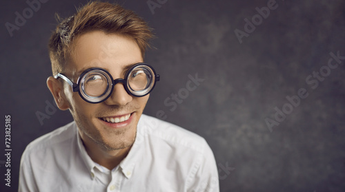 Closeup studio portrait of funny nerd wearing retro vintage thick rimmed glasses on copyspace background. Happy young man in uncool old-fashioned round frame spectacles looking at camera and smiling photo