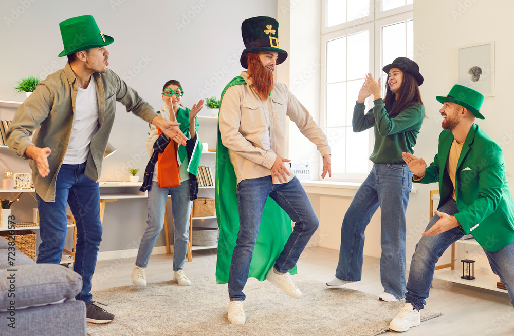 Happy smiling young people friends men and women in funny green clothes and hats having party and dancing having fun in the living room at home celebrating Saint Patrick's Day together.