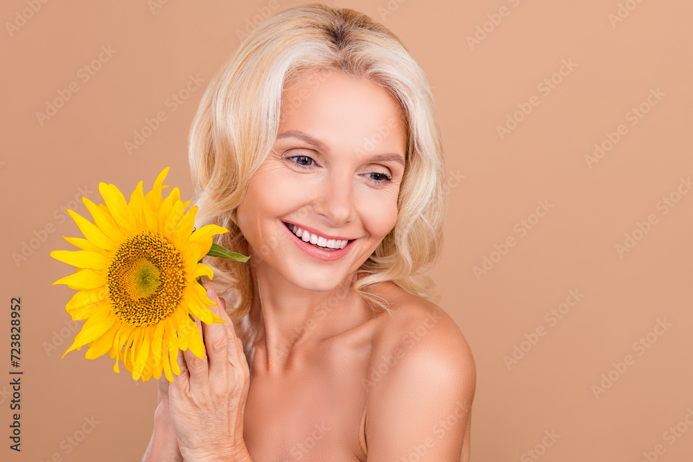 Photo of cheerful lovely adorable retired lady looking empty space beauty novelty product isolated on beige color background Photo of cheerful lovely adorable retired lady looking empty space beauty novelty product isolated on beige color background