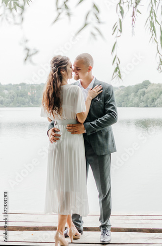 the bride and groom embrace and kiss on the shore of the lake