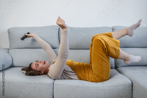 Happy woman lying on her back on the sofa with a smart phone in her hand photo