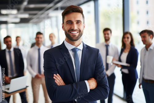 Photo of young office worker man smiling at camera in front of people in suits