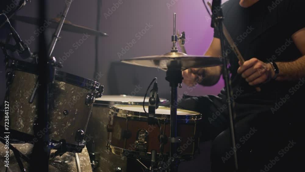 A young Caucasian man drummer plays in a music studio. Knocks the rhythm into the drum with sticks. Records a track of his rock band. Male hitting drum metal cymbals in repetition studio. Slow motion