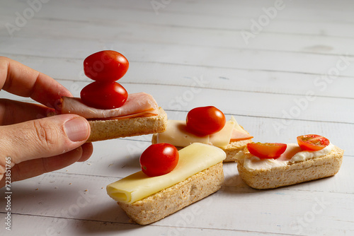 A hand picks up a piece of bread with tomato, cheese, and ham. The mini buns or bread rolls – in Brazil, they are called 'Bisnaguinha. photo