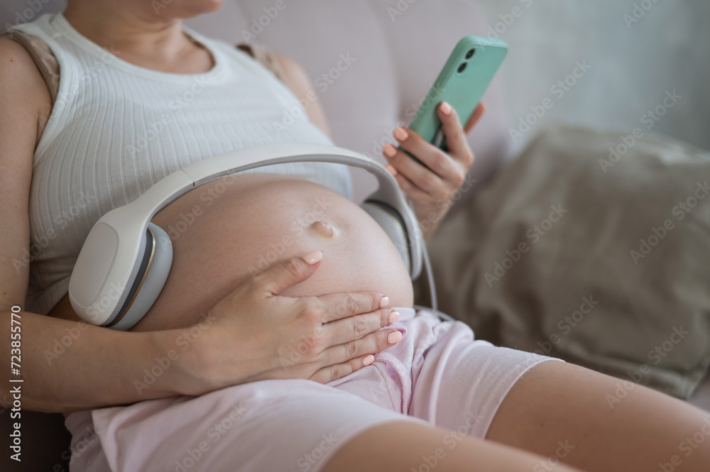 A pregnant woman turns on music for her child on a smartphone. Headphones on the tummy. A pregnant woman turns on music for her child on a smartphone. Headphones on the tummy.