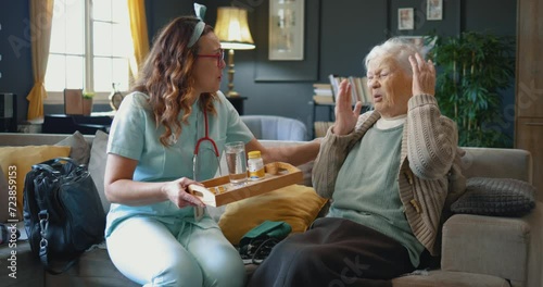 An old retired woman does not want to drink medicine she receives from the caregiver who takes care of her at home. Old female patient refusing to take medicine from nurse photo