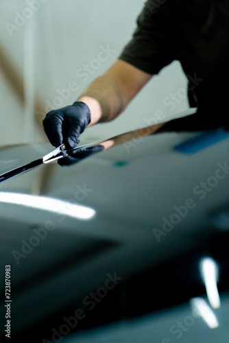 a mechanic tears off excess pieces of tinted protective film from a car window at detailing station