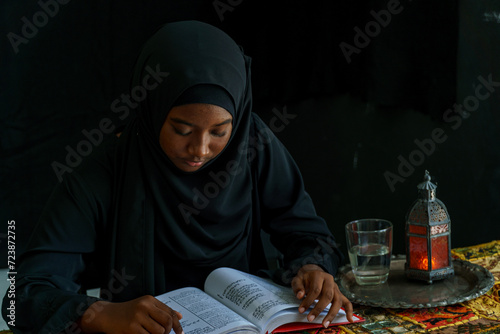 Muslim woman in black hijab Sitting and reading scriptures in a dark room.