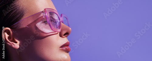 Photography Profile portrait of a beautiful model in trendy square pink sunglasses with glossy make up posing against violet background
