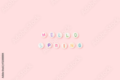 Hello spring. Quote made of white round beads with colorful letters on a pink background. © rorygezfresh