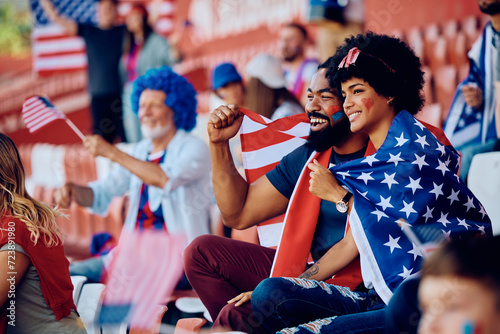Happy black couple wrapped in USA national flag watching sport match stadium.