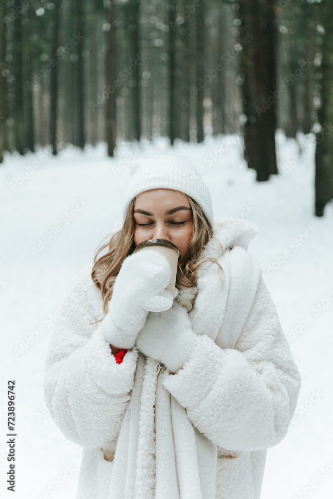 Blonde woman in winter forest or park warming with hot beverage in paper cup Blonde woman in winter forest or park warming with hot beverage in paper cup