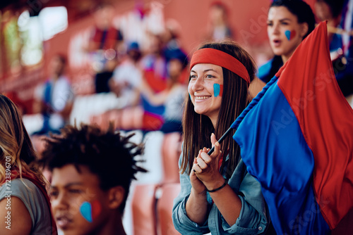 Happy female sports fan with flag at stadium stands.