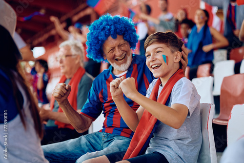 Happy kid watching sports match with his grandfather at stadium. photo