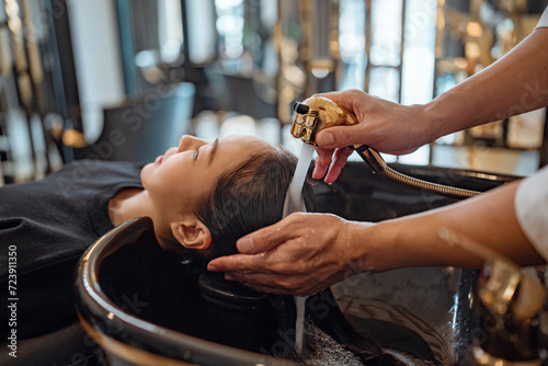 Asian woman lying down on salon washing bed getting hair washed in hair salon by stylist, Hairdresser shampoo the customer hair then washing hair