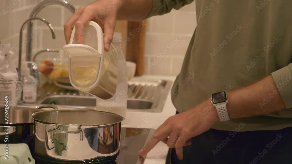 Tilt up shot of bearded man putting semolina into cooking pot with milk standing on induction stove in kitchen Tilt up shot of bearded man putting semolina into cooking pot with milk standing on induction stove in kitchen