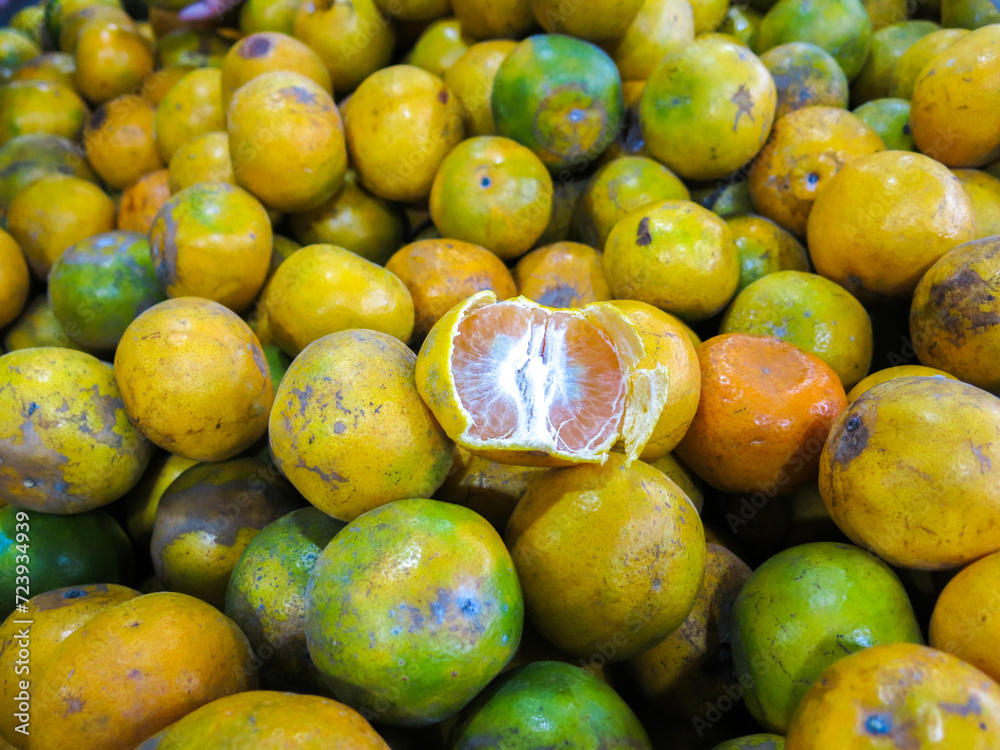 An opened orange fruit on a pile of the fruits. Served as tester for customers so they will buy. Sweet and ripe.