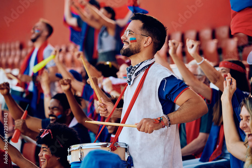 Happy sports fan plays drums while watching match at stadium.