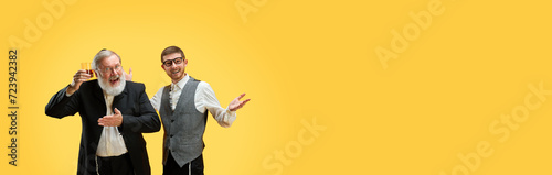 Banner. Two positive young and senior men posing in formal suits against yellow background with negative space to insert text. Purim, business, festival, holiday, celebration concept. Ad