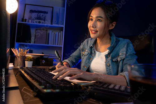 Smiling young beautiful asian creative officer looking on pc in sales target online, earning job's freelancer for planning invest new strategy marketing online planning at neon light night. Stratagem.