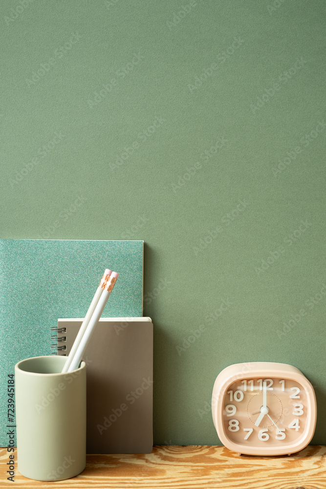 Stationery office supply. Notebook, pencil holder, clock on wooden desk. green wall background. workspace