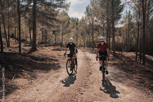 Two professional women cyclists riding gravel bicycles on a gravel road on a sunny summer day. Group bike ride in the natural countryside. Gravel advanture. Gravel cycling adventure. Alicante, Spain .