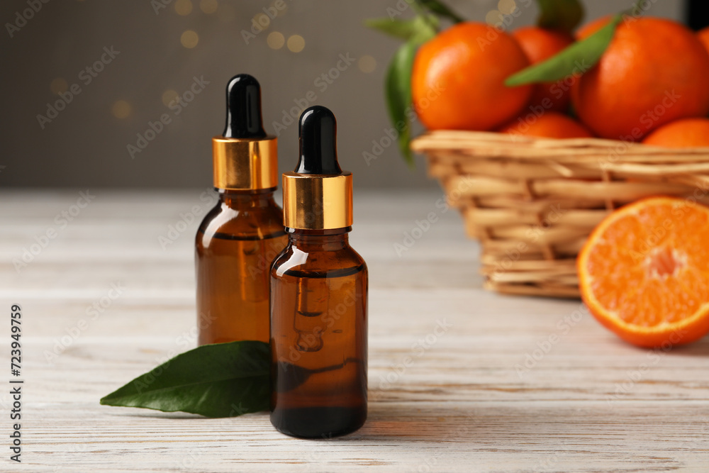 Bottles of tangerine essential oil and green leaf on white wooden table, closeup Bottles of tangerine essential oil and green leaf on white wooden table, closeup