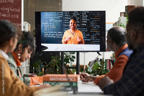 Black woman as professor on computer screen giving online class via remote technology to group of students photo
