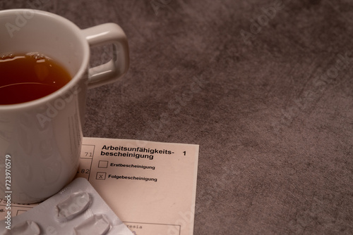 Eine Tasse Tee neben Medikamenten und einer Arbeitsunfähigkeitsbescheinigung auf grauem Untergrund, Studioaufnahme, Deutschland