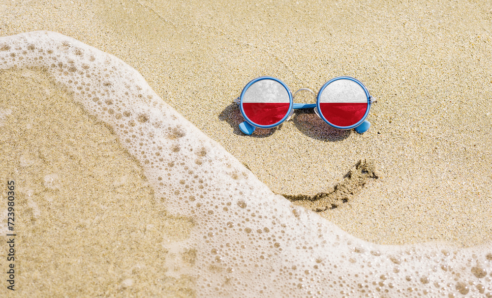 Sunglasses with flag of Poland on a sandy beach. Nearby is a sea lightning and a painted smile. The concept of a successful vacation in the resorts of Poland.