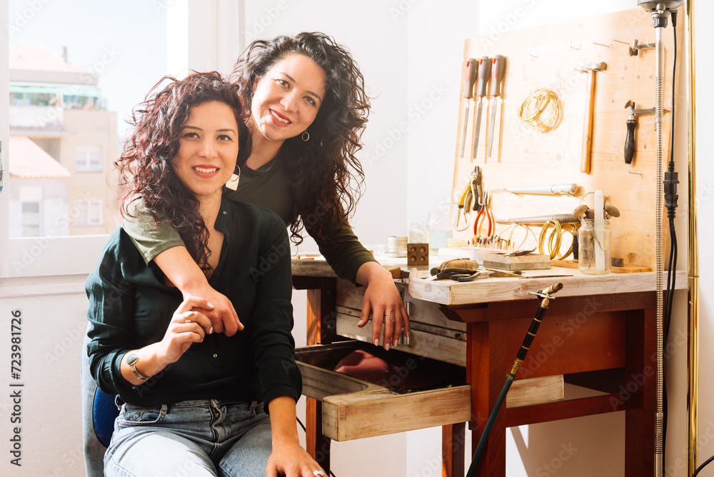 Happy twin sisters hugging over back in jewellery workshop Happy twin sisters hugging over back in jewellery workshop