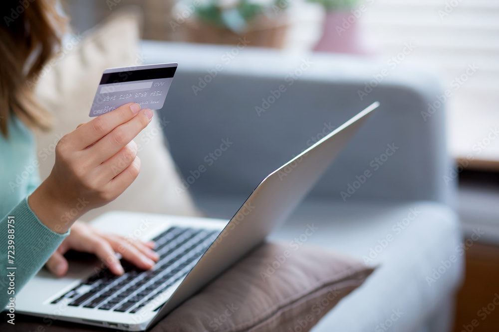 Young asian woman sitting on sofa using laptop computer shopping online with credit card buying to internet, female payment with business on couch, purchase and payment, business and lifestyles.
