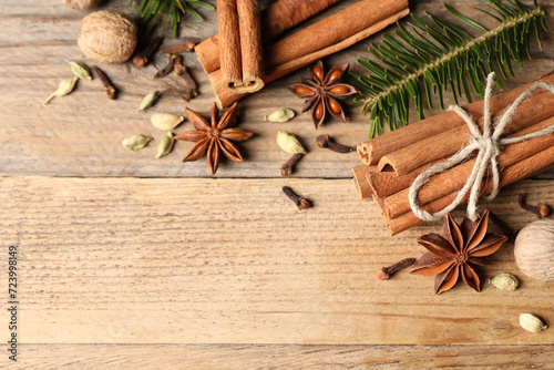 Different aromatic spices and fir branches on wooden table, flat lay. Space for text