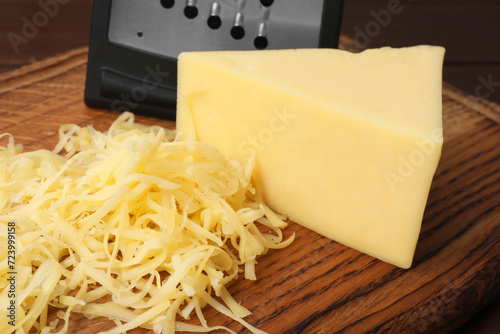 Grated and whole piece of cheese on wooden board, closeup