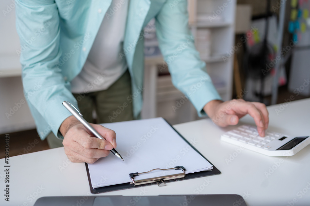 Business professional using a calculator and taking notes, financial planning or budgeting on a clipboard in an office. Business professional using a calculator and taking notes, financial planning or budgeting on a clipboard in an office.