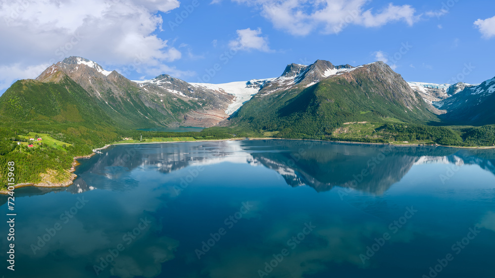 The tranquil fjord perfectly mirrors the towering Saltfjell mountains and the receding Svartisen Glacier, a natural marvel under the soft glow of the Scandinavian sun