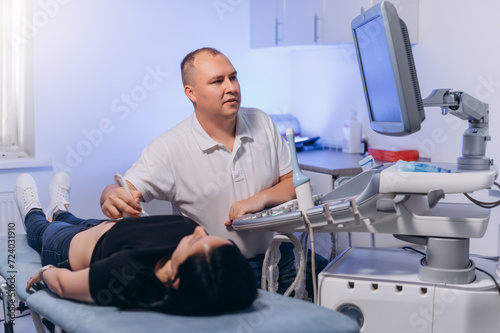 A male doctor performs an abdominal ultrasound on a female patient in the clinic. Pregnant woman at a gynecologist s appointment.