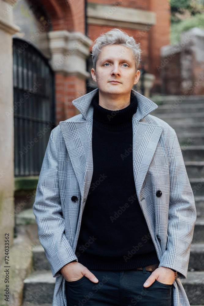 Handsome male model with gray hair in a black roll neck jacket and trousers, checked coat walking on the old city street. Cold season fashion stylish outfit trend. Old money aesthetic. Soft focus. Handsome male model with gray hair in a black roll neck jacket and trousers, checked coat walking on the old city street. Cold season fashion stylish outfit trend. Old money aesthetic. Soft focus.