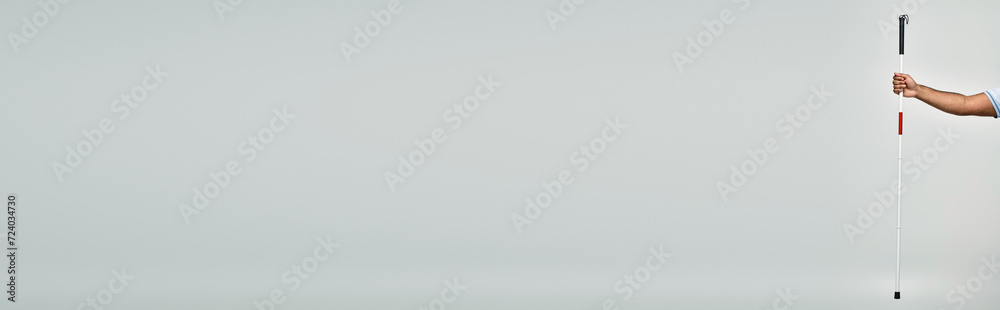 cropped view of blind indian man in blue t shirt holding his walking stick on gray backdrop, banner