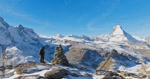 Panoramic landscape of Young man backpacker take a photo by camera at Switzerland mountain peak view point with iconic famous landscape Matterhorn background. Nature, Travel and Adventure concept.