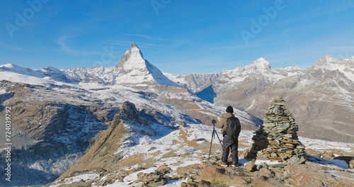 Panoramic landscape of Young man backpacker take a photo by camera at Switzerland mountain peak view point with iconic famous landscape Matterhorn background. Nature, Travel and Adventure concept.