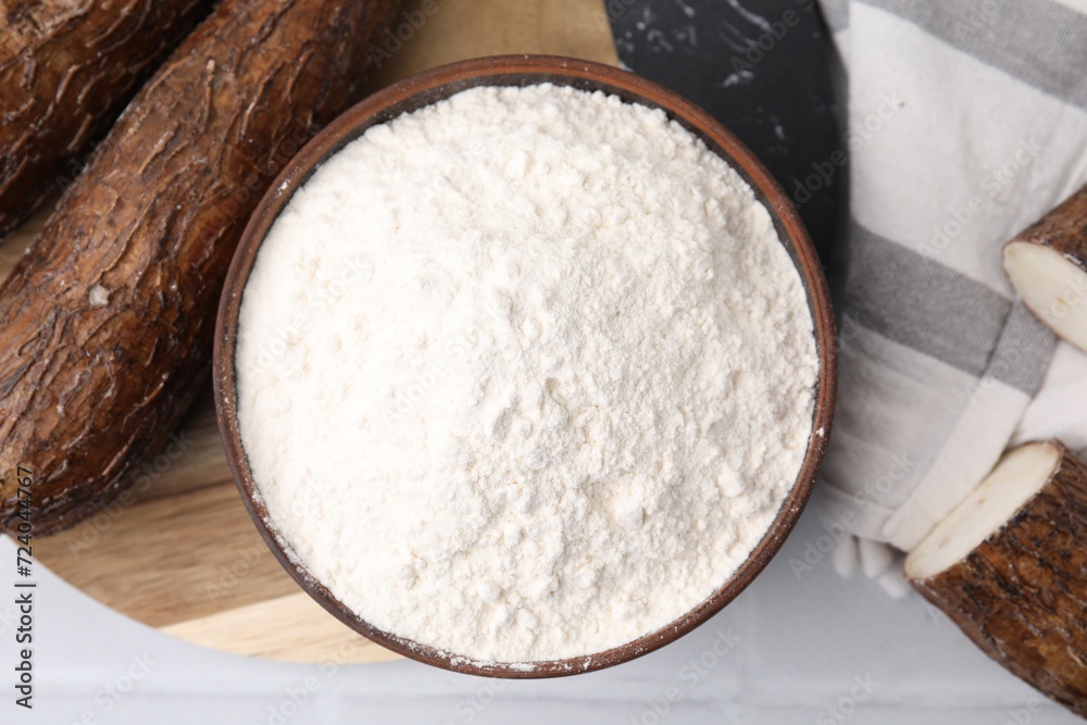 Bowl with cassava flour and roots on white table, top view Bowl with cassava flour and roots on white table, top view