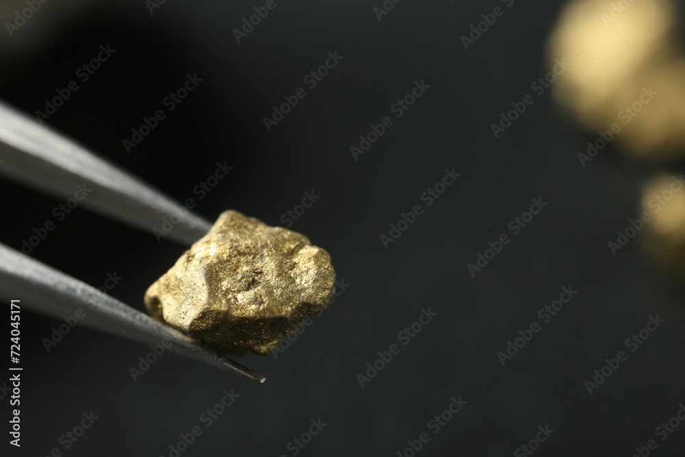 Tweezer with shiny gold nugget on blurred background, closeup. Space for text Tweezer with shiny gold nugget on blurred background, closeup. Space for text