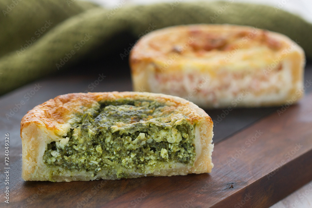 spinach and cheese quiche on a dark wooden board, with a green cloth for production and rustic white wooden background, horizontal photography, focus on sliced spinach quiche