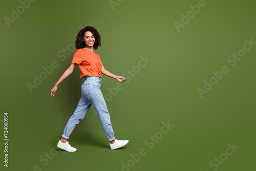 Full length photo of excited positive lady dressed orange t-shirt walking empty space isolated khaki color background