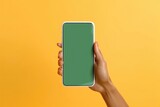 Modern bezel-less smartphone with blank green screen on hand isolated on yellow background