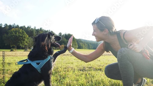 SLOW MOTION: Attractive young woman smiling while enjoying time outdoors with her pet dog. Positive dog training fun trick. Owner high five with dog paw. Lens flare low angle