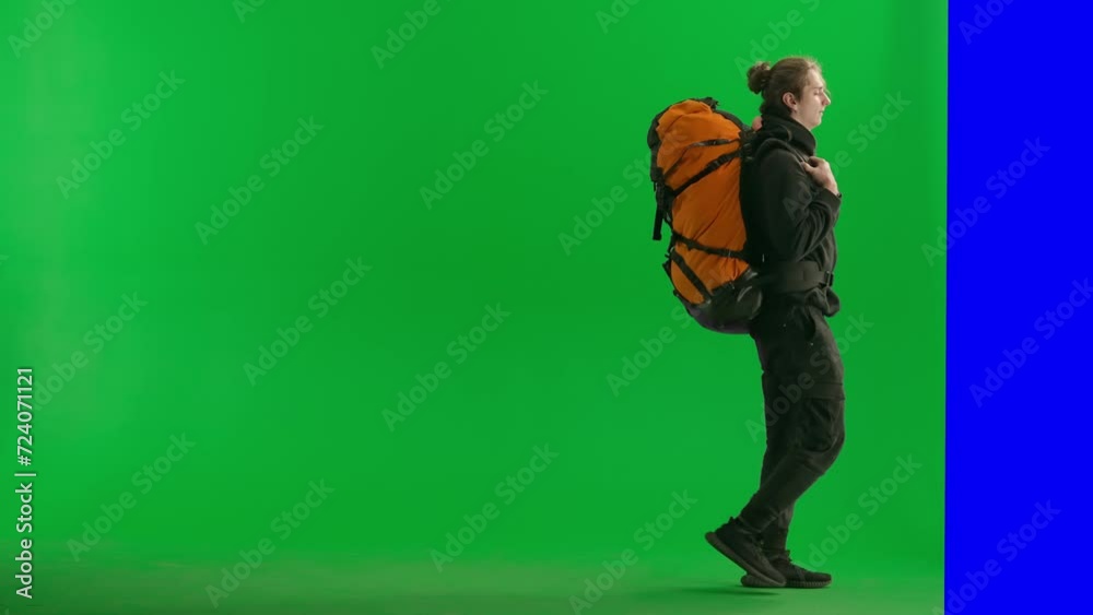 Side view of a male hiker walking, jumping over an obstacle and disappearing behind a screen. Man with hiking backpack in studio on green screen. Side view of a male hiker walking, jumping over an obstacle and disappearing behind a screen. Man with hiking backpack in studio on green screen.