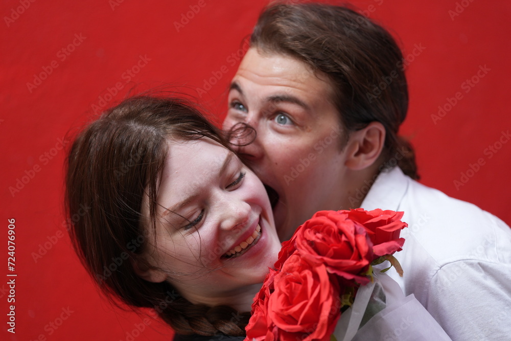 couple young man and woman hugging and holding the red bouquet rose flowers at red wall background. Concept couple life with love and happy moment. couple young man and woman hugging and holding the red bouquet rose flowers at red wall background. Concept couple life with love and happy moment.