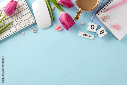 Femininity flourishes: a workday tribute to women on their day. Top view shot of keyboard, computer mouse, cube calendar, coffee, hearts, notebooks, tulips on pastel blue background with advert area photo